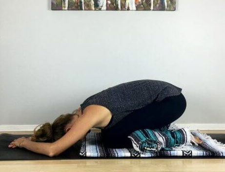woman doing yoga pose with blanket under knees